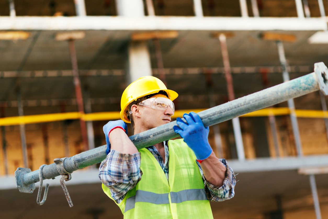 Worker carrying steel support bars on construction site