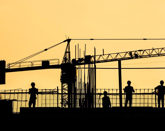 silhouette of workmen and crane against a yellow sky