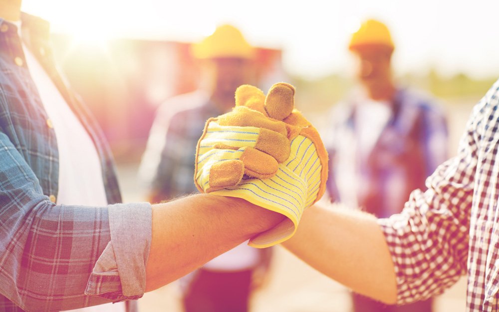 Two workmen clasp hands with gloves on